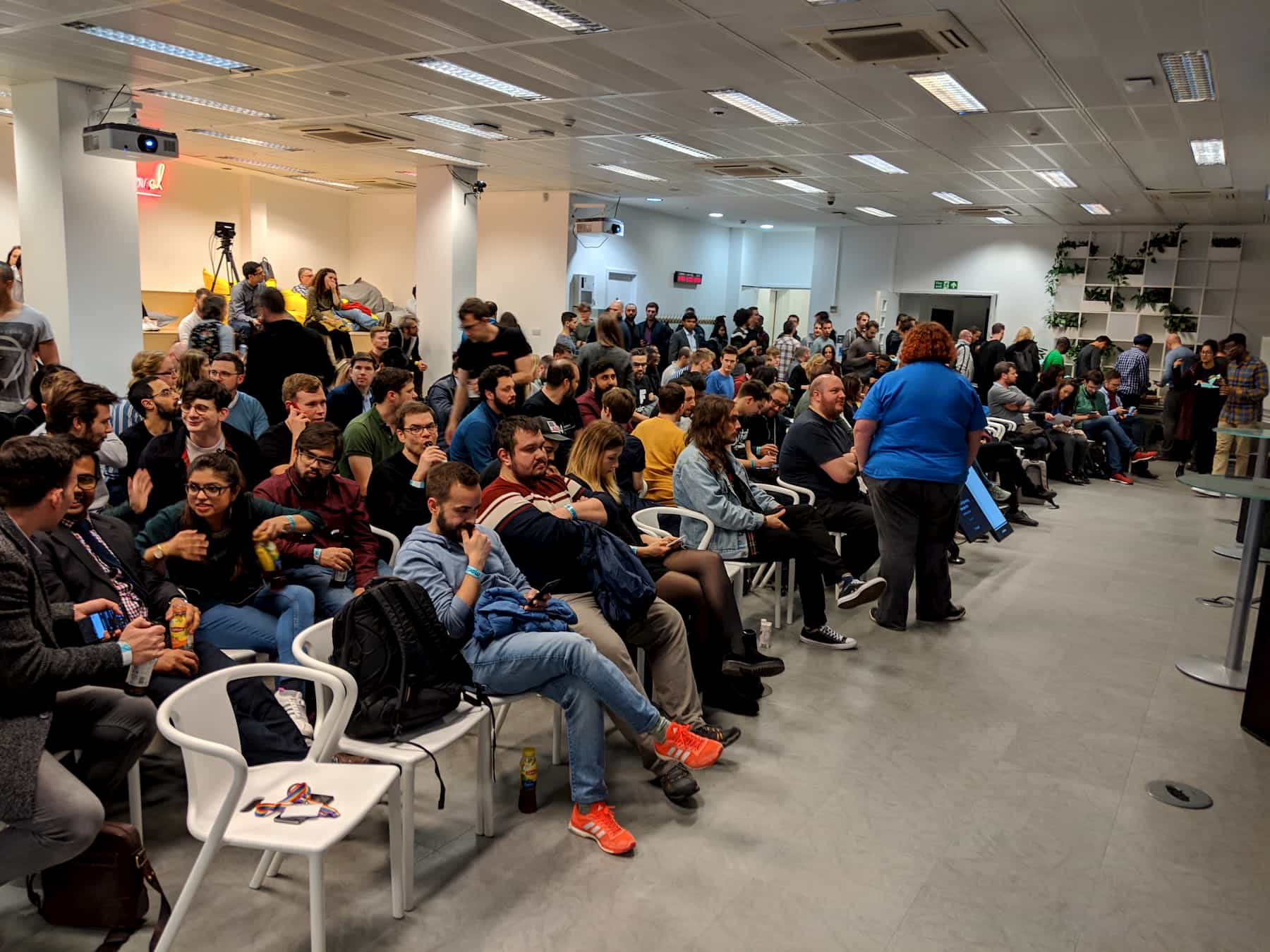 A full room containing around 200 people, all sat on rows of chairs and benches facing the right