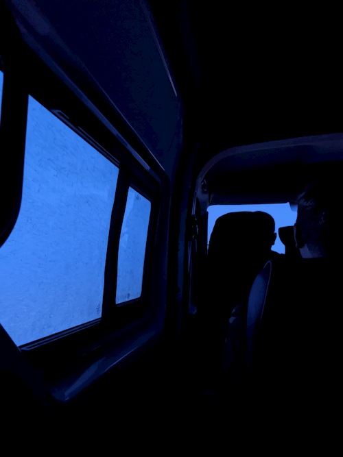 A dark interior of a van with shadows, with snow outside