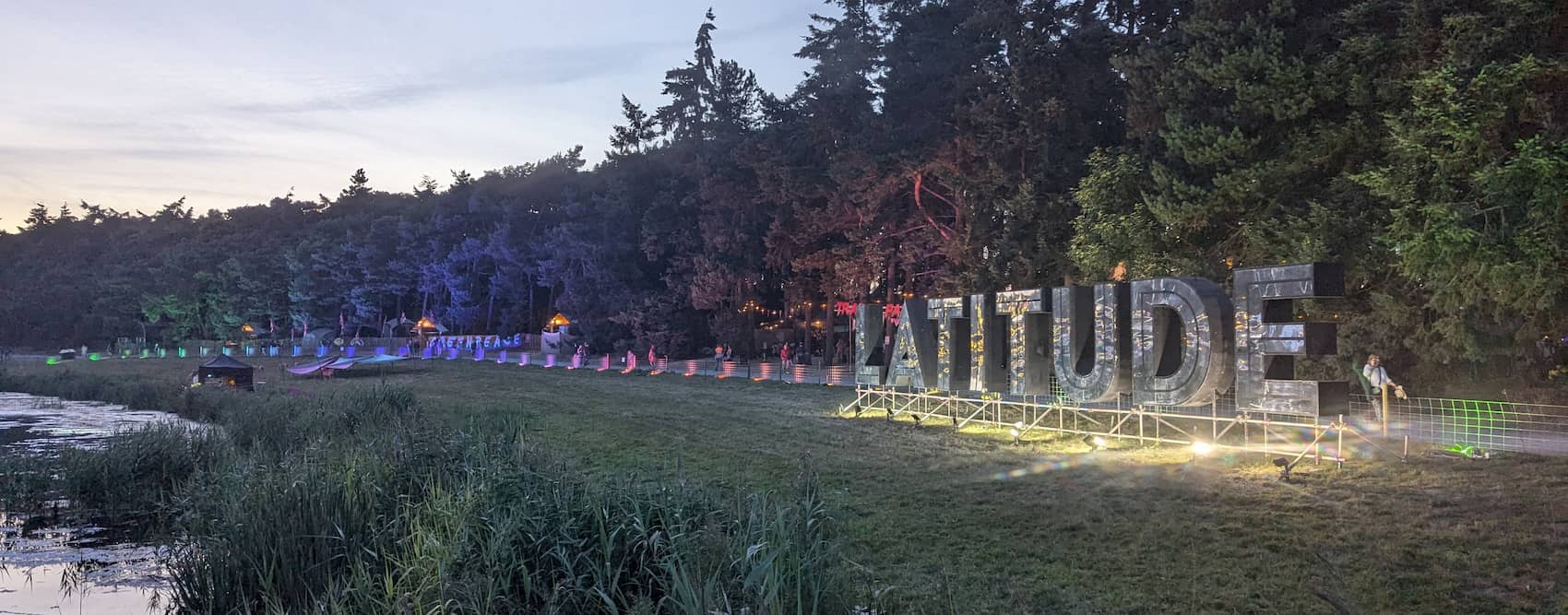 A landscape showing the river that flows through the latitude site, along with big shiny letters spelling out LATITUDE. It's getting dark and there's rainbow lighting