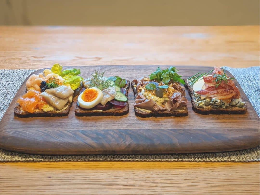 A row of four Smørrebrød open sandwiches on a wood board